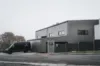 Ein graues Gebäude vor dem ein Transporter steht.