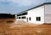 Lagerhalle von vorne. Die Halle sieht fertig aus, die Erde drumherum ist noch karg mit Baggerspuren.