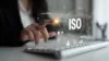 Hand über einer Tastatur mit einer Holographischen Darstellung von Symbolen. Zentral das Wort ISO